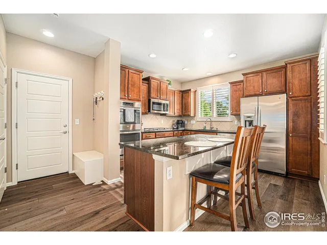 a open kitchen with stainless steel appliances granite countertop a refrigerator a sink dishwasher a dining table and chairs with wooden floor