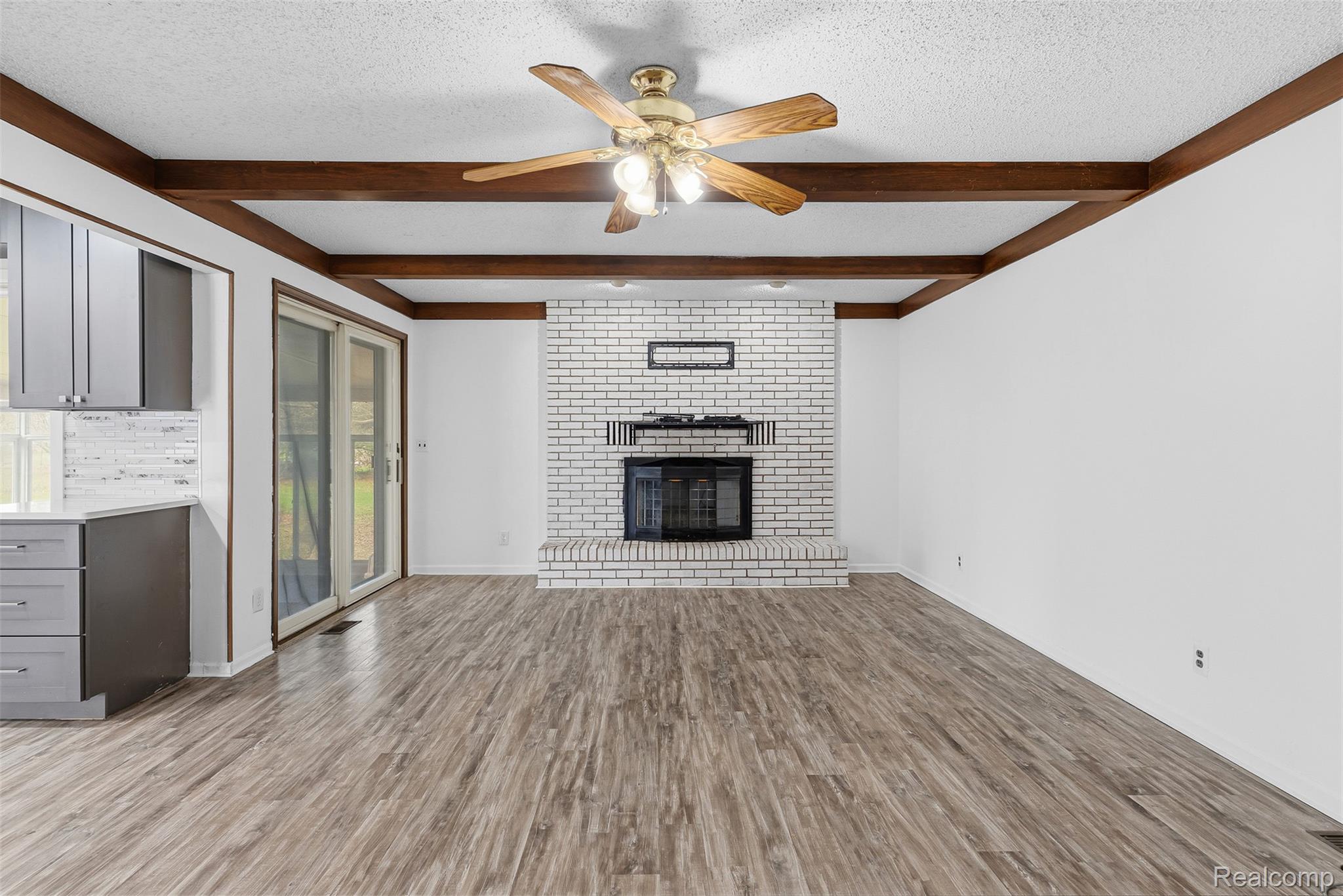 3432 South State Road Davison, MI 48423 - Photo 31 of 58 Unfurnished living room featuring a textured ceiling, a ceiling fan, light wood-style flooring, a fireplace, and beamed ceiling