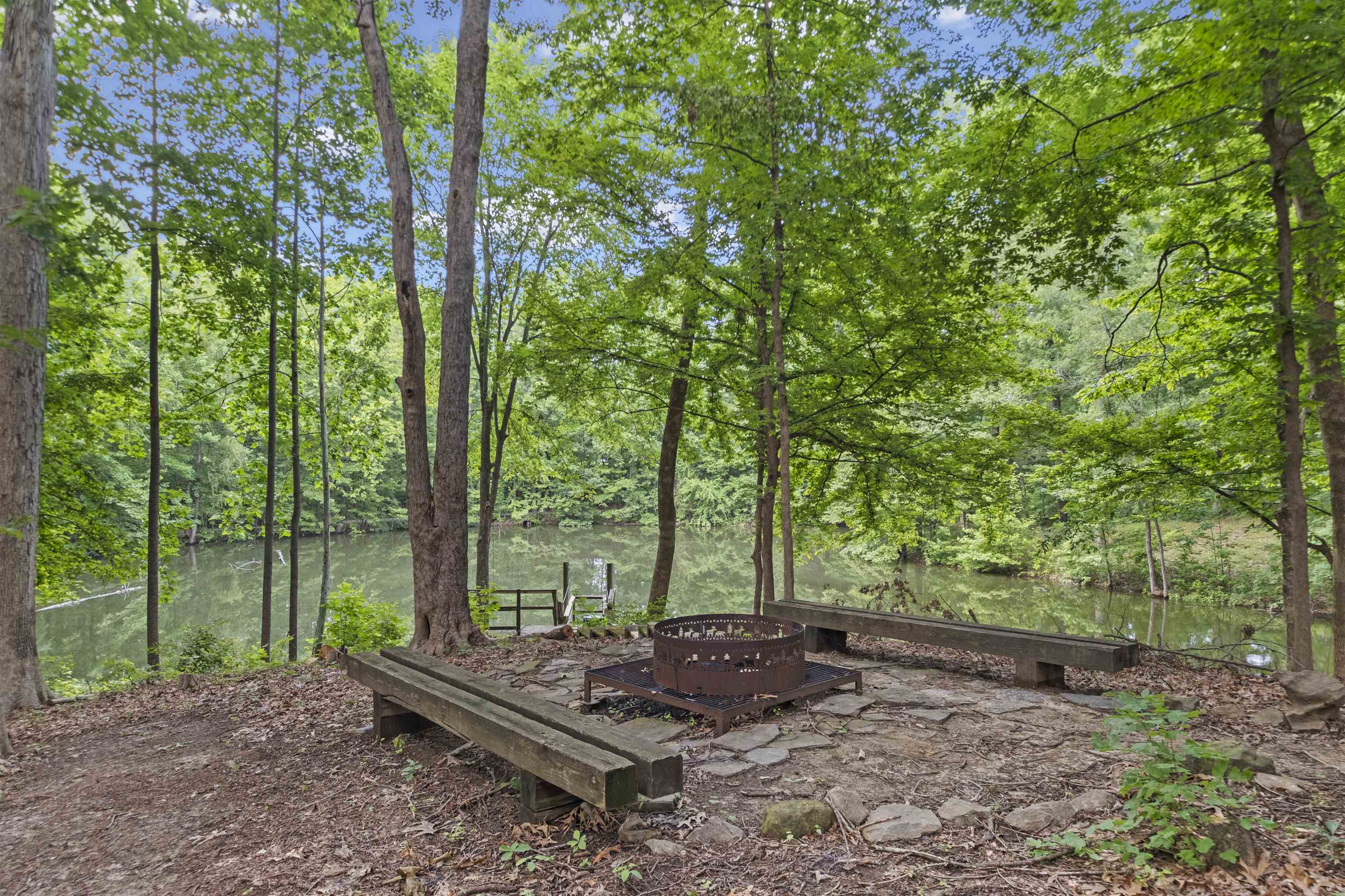 3601 Marshall Road Munford, TN 38058 - Photo 7 of 35 Lakeside fire pit area featuring a stone and dirt base, two long wooden benches, and mature trees