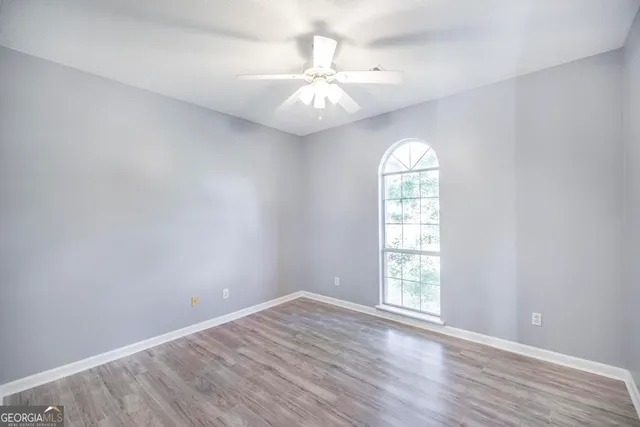 an empty room with wooden floor chandelier fan and windows