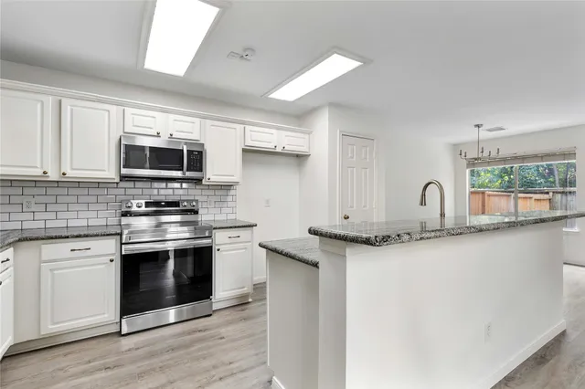 a kitchen with granite countertop a sink stainless steel appliances and white cabinets