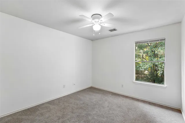 an empty room with a chandelier fan and windows