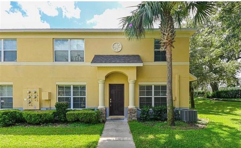 a view of a brick house with a yard plants and palm trees