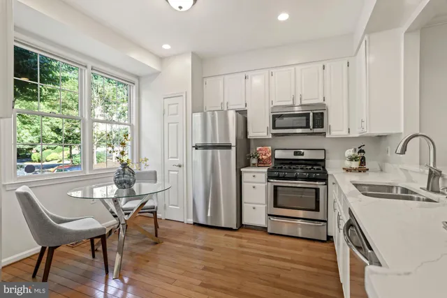 a kitchen with stainless steel appliances granite countertop a stove a refrigerator a sink dishwasher a dining table and chairs with wooden floor