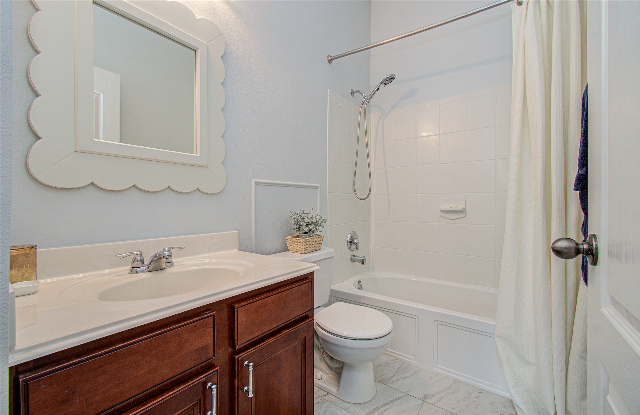 20007 Alcea Court Spring, TX 77379 - Photo 27 of 36 This bathroom features a clean design with a white tile shower-tub combo, a marble countertop with a modern faucet, and rich wooden cabinetry. A decorative mirror and soft lighting enhance the space, providing a welcoming, functional feel.
