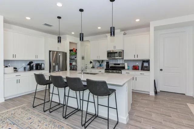 a kitchen with stainless steel appliances kitchen island a refrigerator a stove a sink and white cabinets with wooden floor