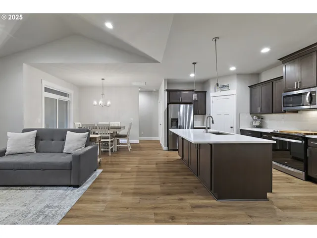 a living room with stainless steel appliances kitchen island granite countertop a table chairs and a refrigerator