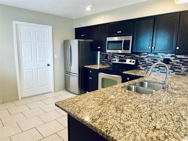 a kitchen with kitchen island granite countertop a sink a stove a microwave a refrigerator and white cabinets