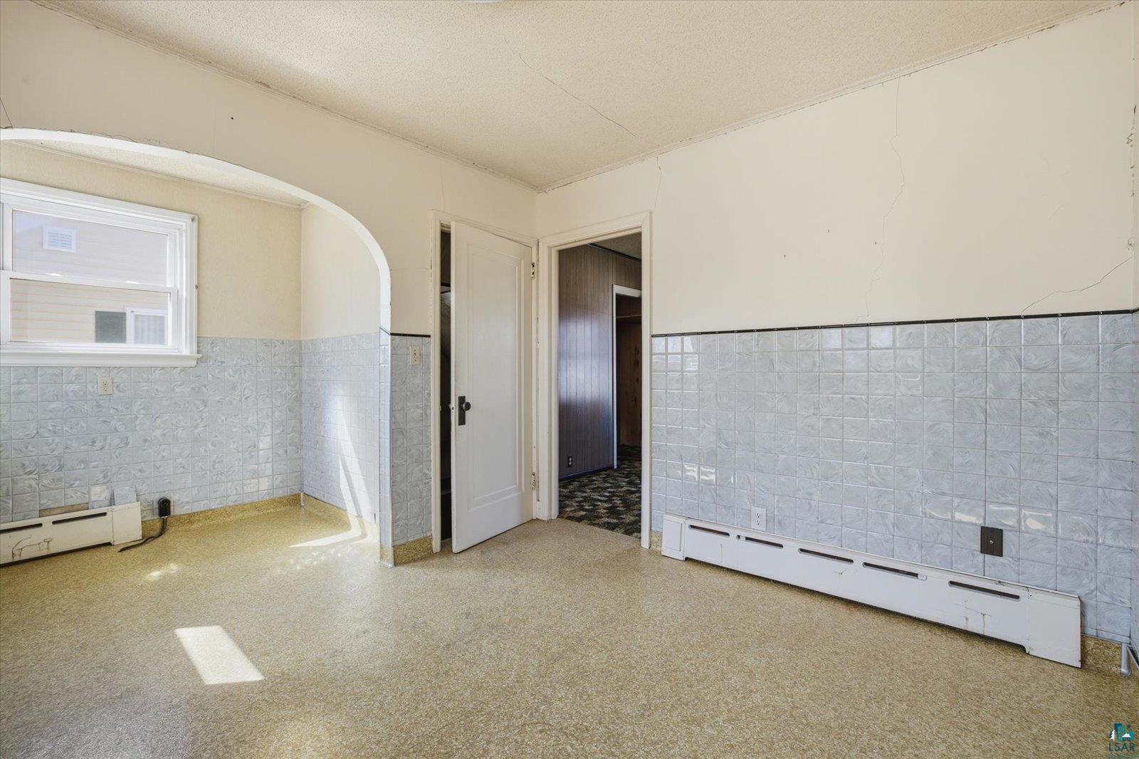 709 Michigan Street Hibbing, MN 55746 - Photo 33 of 47 Spare room featuring tile walls, a wainscoted wall, baseboard heating, and a textured ceiling