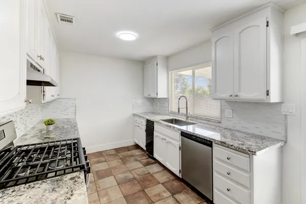 a kitchen with granite countertop a sink a stove and cabinets