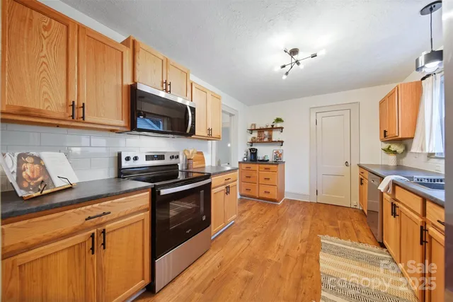 a kitchen with stainless steel appliances granite countertop a sink a stove top oven a refrigerator with grey cabinets and wooden floor