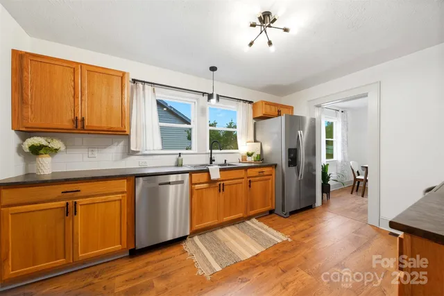 a large kitchen with stainless steel appliances granite countertop a refrigerator a sink dishwasher a dining table and chairs with wooden floor