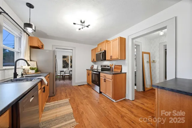 a kitchen with granite countertop a stove top oven a sink dishwasher a refrigerator and a dining table with wooden floor