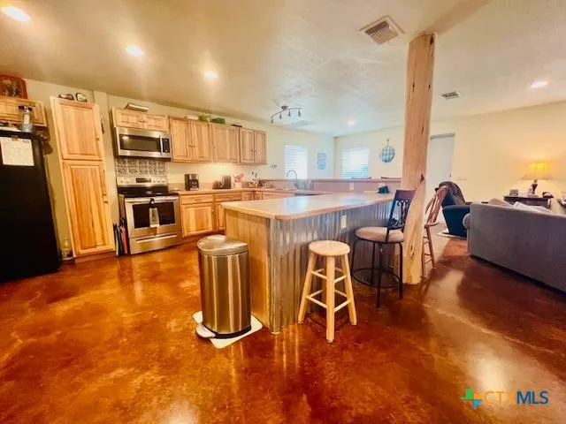 a kitchen with stainless steel appliances granite countertop a refrigerator a stove a sink a dining table and chairs with wooden floor