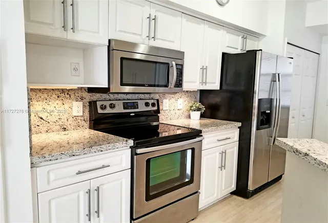 a kitchen with granite countertop white cabinets and stainless steel appliances