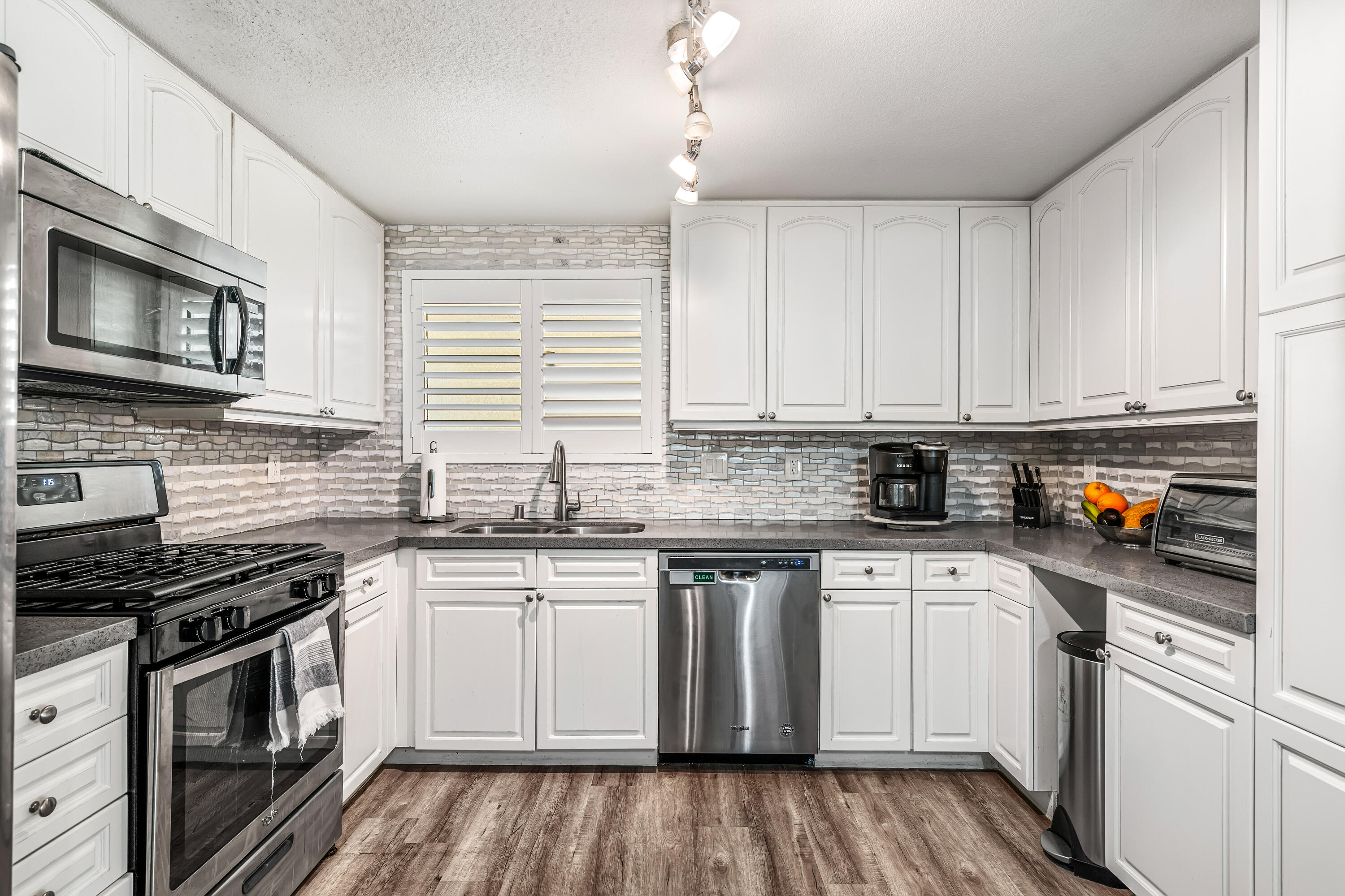67265 Rango Road Cathedral City, CA 92234 - Photo 19 of 49 a kitchen with stainless steel appliances granite countertop a stove top oven a sink dishwasher and white cabinets with wooden floor