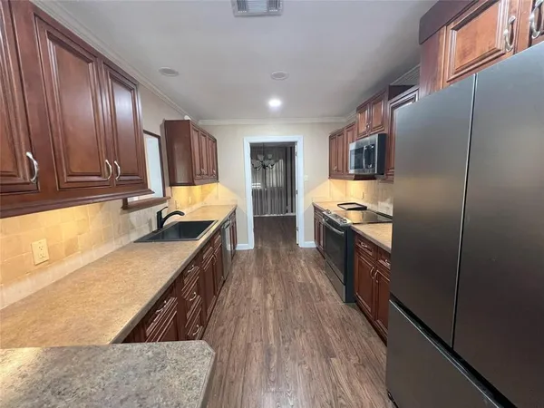 a kitchen with stainless steel appliances granite countertop a refrigerator a stove top oven a sink dishwasher and wooden cabinets with wooden floor
