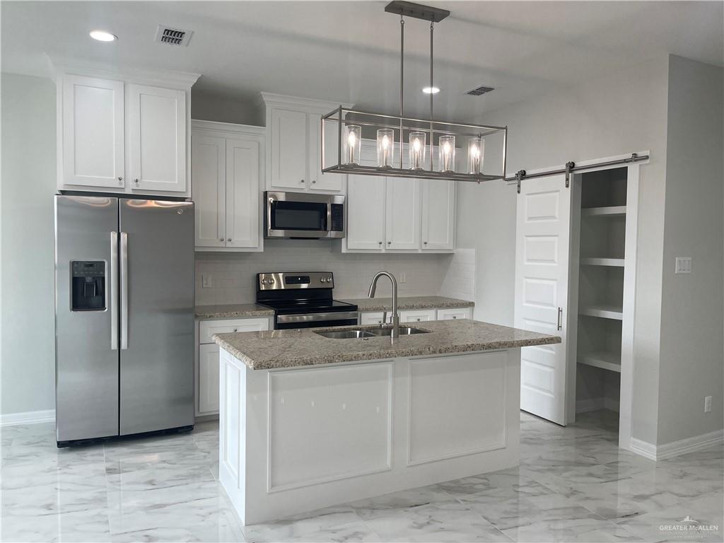 5515 North Crown Point Pharr, TX 78577 - Photo 5 of 15 Kitchen featuring appliances with stainless steel finishes, decorative backsplash, white cabinetry, a barn door, and recessed lighting