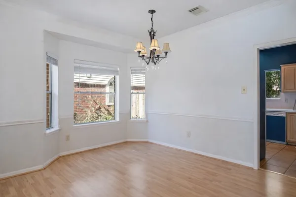 an empty room with wooden floor chandelier and windows