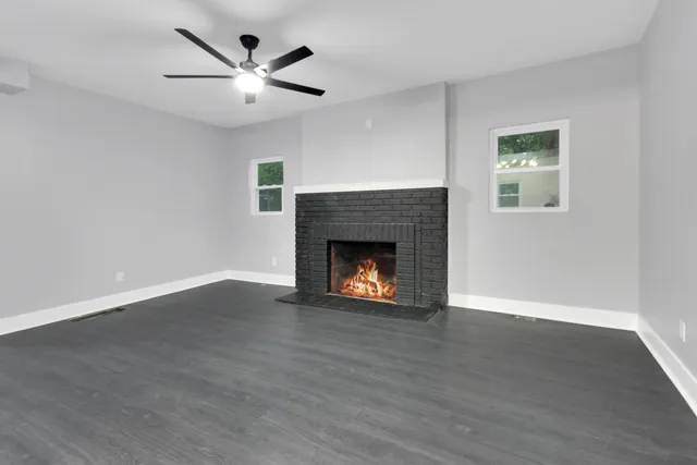 a view of an empty room with wooden floor a fireplace and a window