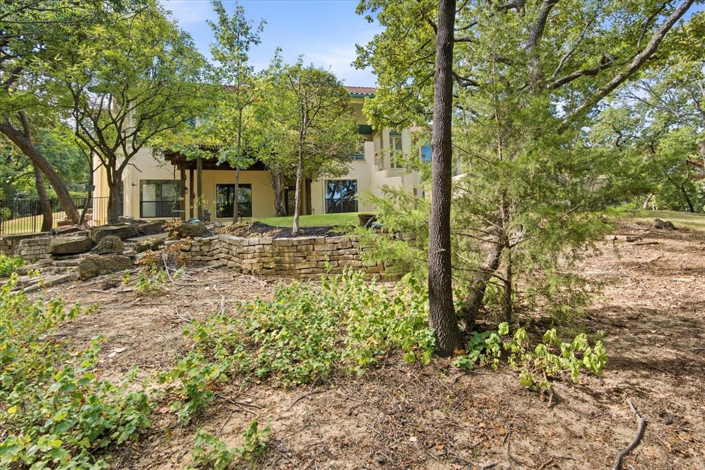 3606 Labrador Grapevine, TX 76051 - Photo 16 of 38 Stucco exterior with multiple windows, covered patio, and natural landscaping with mature trees and stone retaining walls