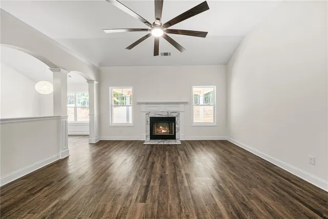 an empty room with wooden floor a ceiling fan a fireplace and windows