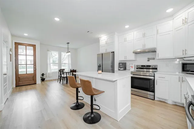 a kitchen with stainless steel appliances granite countertop a stove a sink a refrigerator and white cabinets with wooden floor