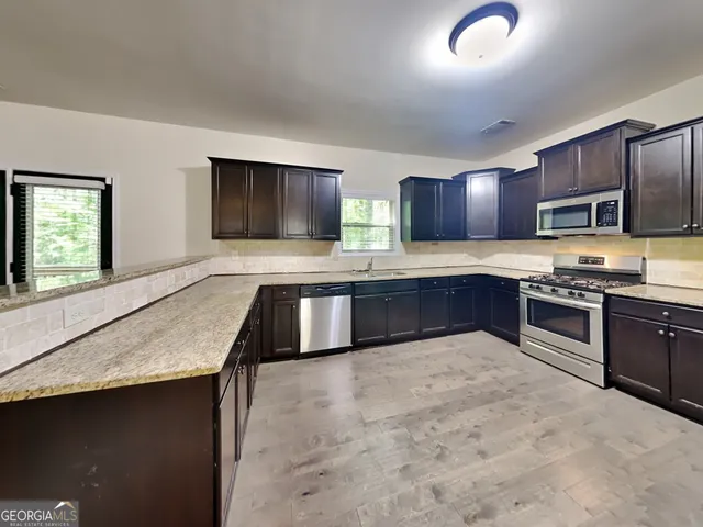 a large kitchen with stainless steel appliances granite countertop a stove a sink and a microwave
