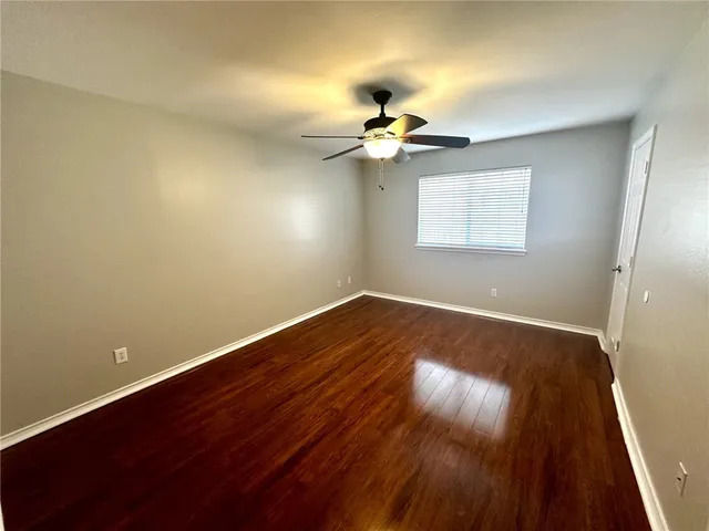 an empty room with wooden floor fan and windows