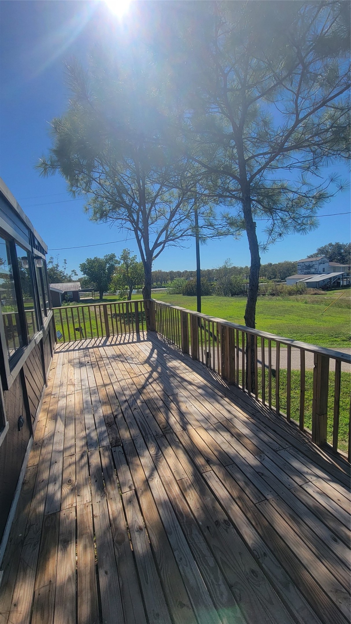 12018 Sandpiper Road Angleton, TX 77515 - Photo 6 of 48 This photo showcases a spacious wooden deck with railing, offering a sunny spot for relaxation. Surrounded by greenery and trees, it provides a serene outdoor space with a view of open land and clear skies.