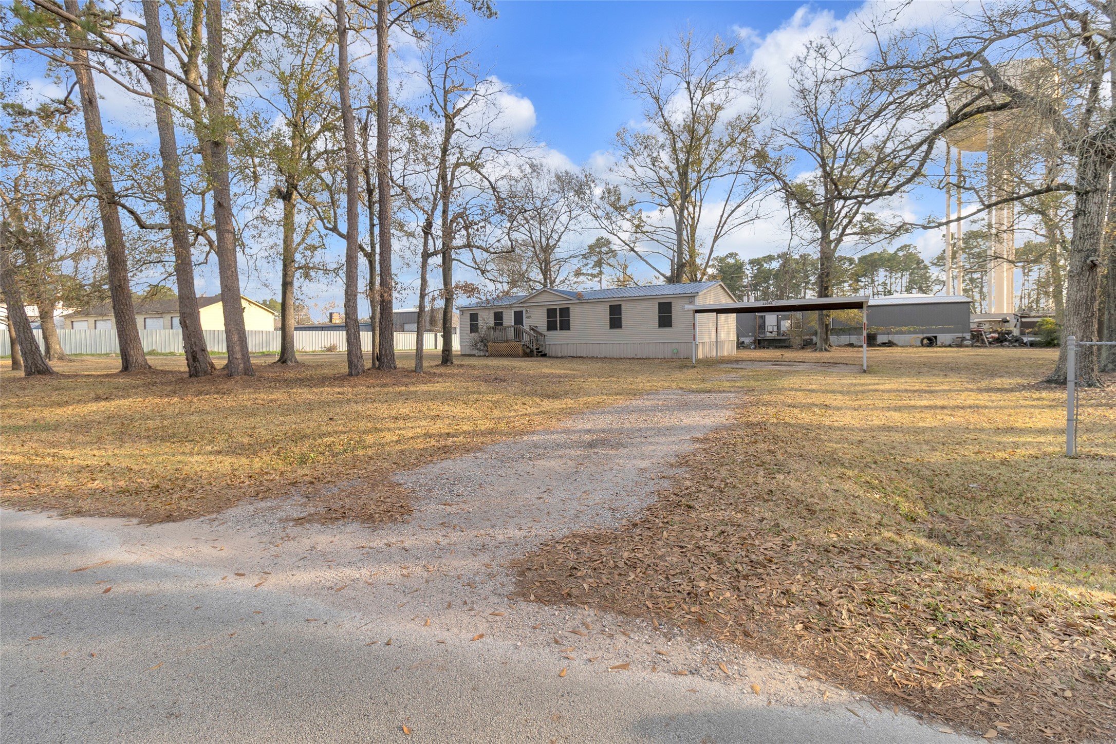 22094 Spear Road Porter, TX 77365 - Photo 38 of 45 Tree-filled yard and a gravel driveway leading up to a carport. The setting is open and peaceful, with a mix of trees and open lawn areas.