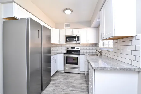 a kitchen with granite countertop a refrigerator a sink a stove top oven and cabinetry