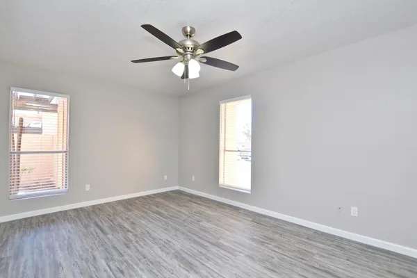 an empty room with wooden floor fan and windows