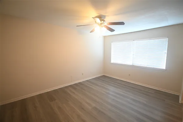 an empty room with wooden floor fan and windows