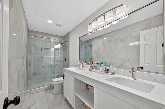 a bathroom with a double vanity sink mirror double shower and a toilet