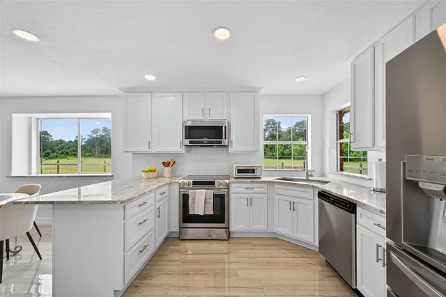 a kitchen with stainless steel appliances granite countertop white cabinets a sink a window and stainless steel appliances