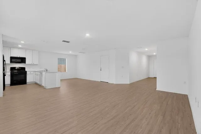 a view of empty room with wooden floor and kitchen