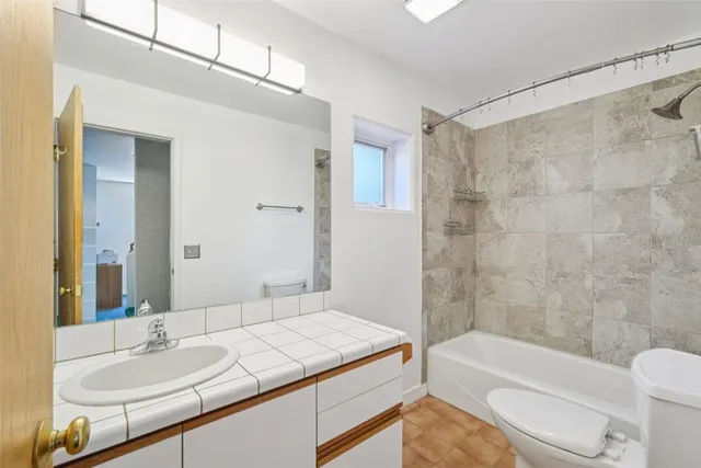 a bathroom with a granite countertop sink a toilet a mirror and bathtub