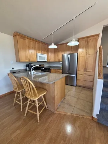 a kitchen with stainless steel appliances granite countertop a refrigerator a sink dishwasher a stove a dining table and chairs with wooden floor