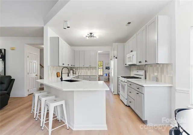 a kitchen with stainless steel appliances kitchen island granite countertop a stove a sink a refrigerator and white cabinets with wooden floor