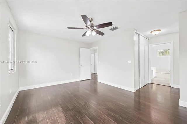 an empty room with wooden floor ceiling fan and windows