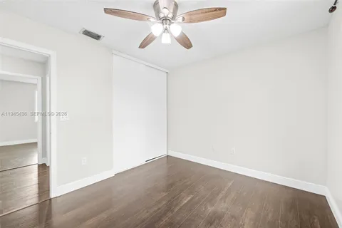 an empty room with wooden floor closet and fan