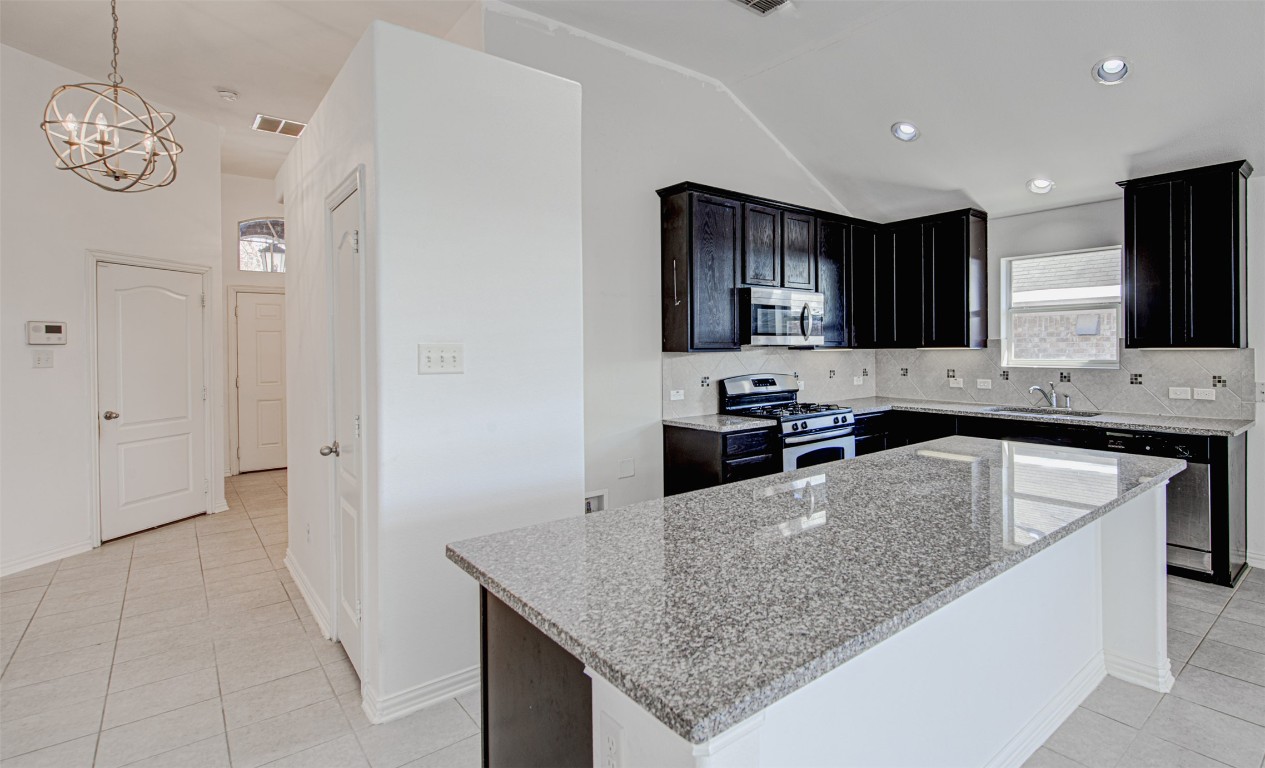239 Pond View Pass Buda, TX 78610 - Photo 3 of 30 Kitchen with light stone countertops, light tile patterned floors, appliances with stainless steel finishes, pendant lighting, and vaulted ceiling