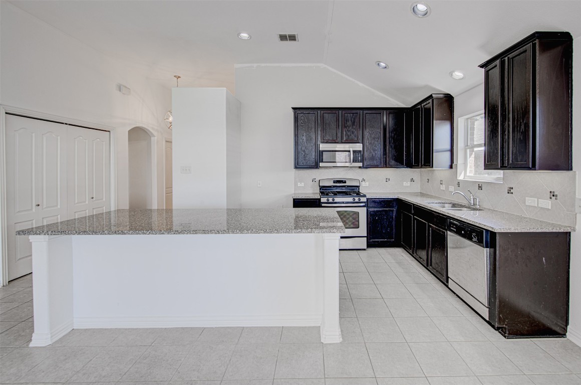 239 Pond View Pass Buda, TX 78610 - Photo 4 of 30 Kitchen with stainless steel appliances, decorative backsplash, a center island, light stone counters, and lofted ceiling