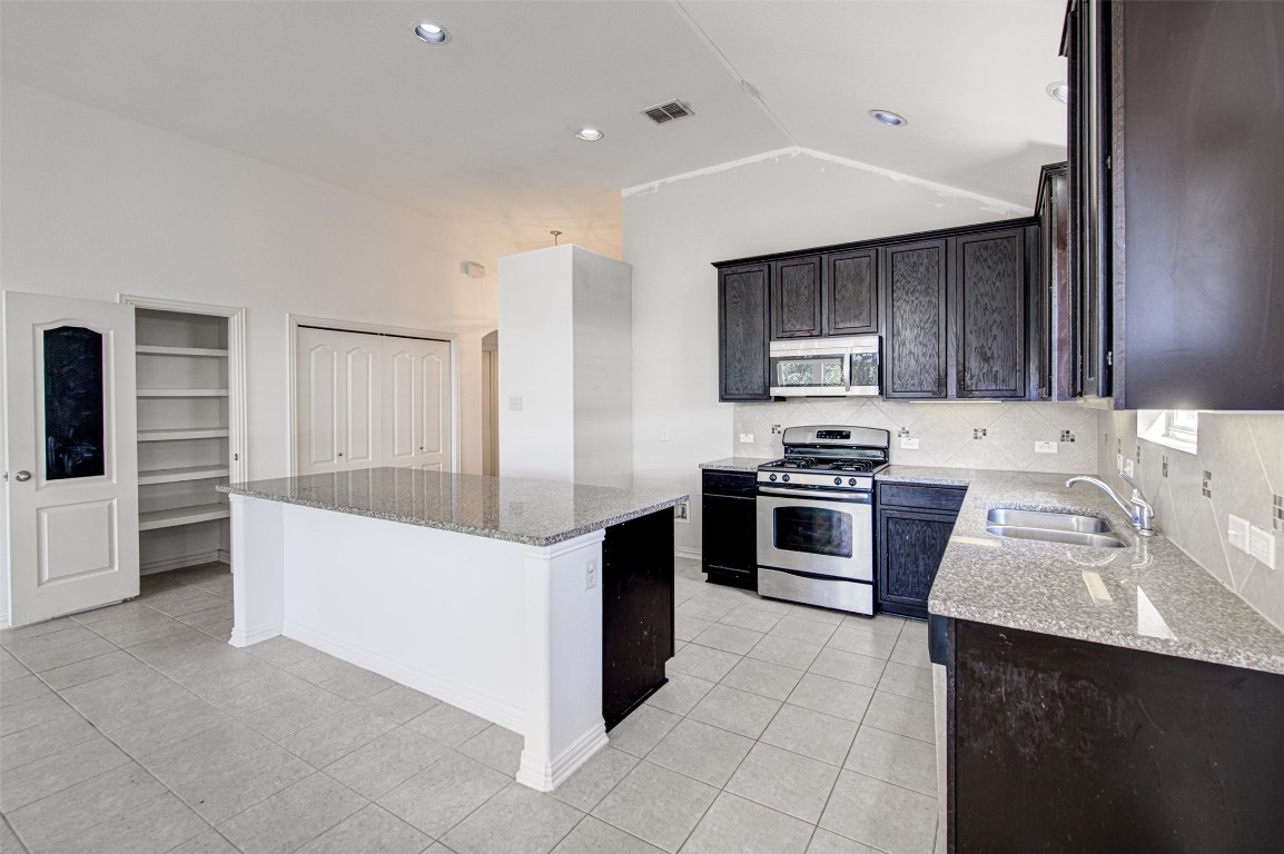 239 Pond View Pass Buda, TX 78610 - Photo 5 of 30 Kitchen featuring light stone countertops, stainless steel appliances, built in shelves, a kitchen island, and light tile patterned floors