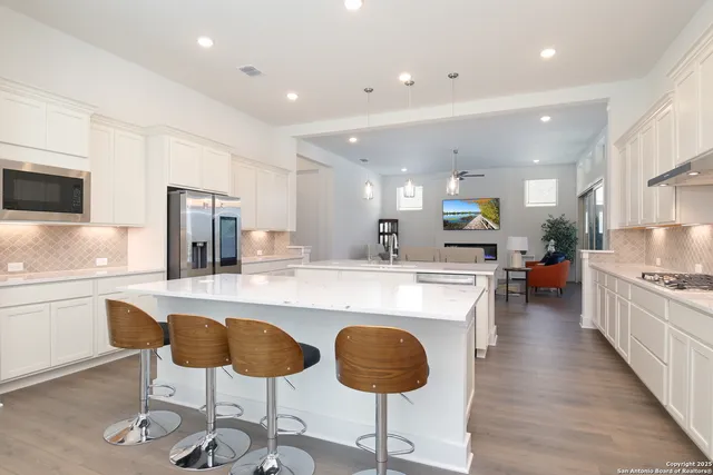 a kitchen with stainless steel appliances granite countertop a stove top oven a refrigerator a sink and white cabinets with wooden floor