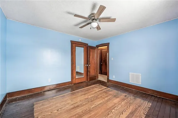 a view of an empty room with wooden floor and a ceiling fan