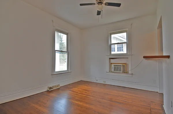 an empty room with wooden floor chandelier fan and windows