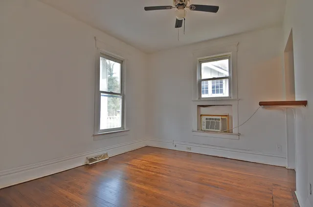 an empty room with wooden floor chandelier fan and windows