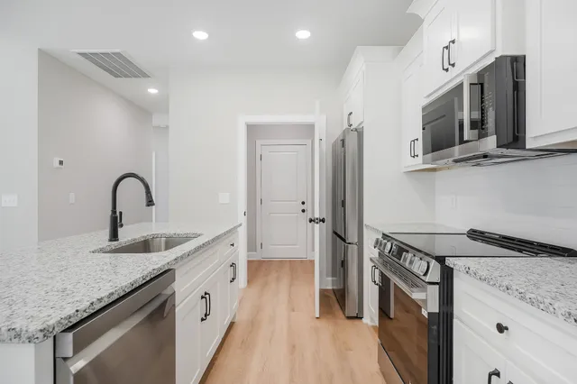 a kitchen with stainless steel appliances granite countertop a sink and a stove top oven with wooden floor